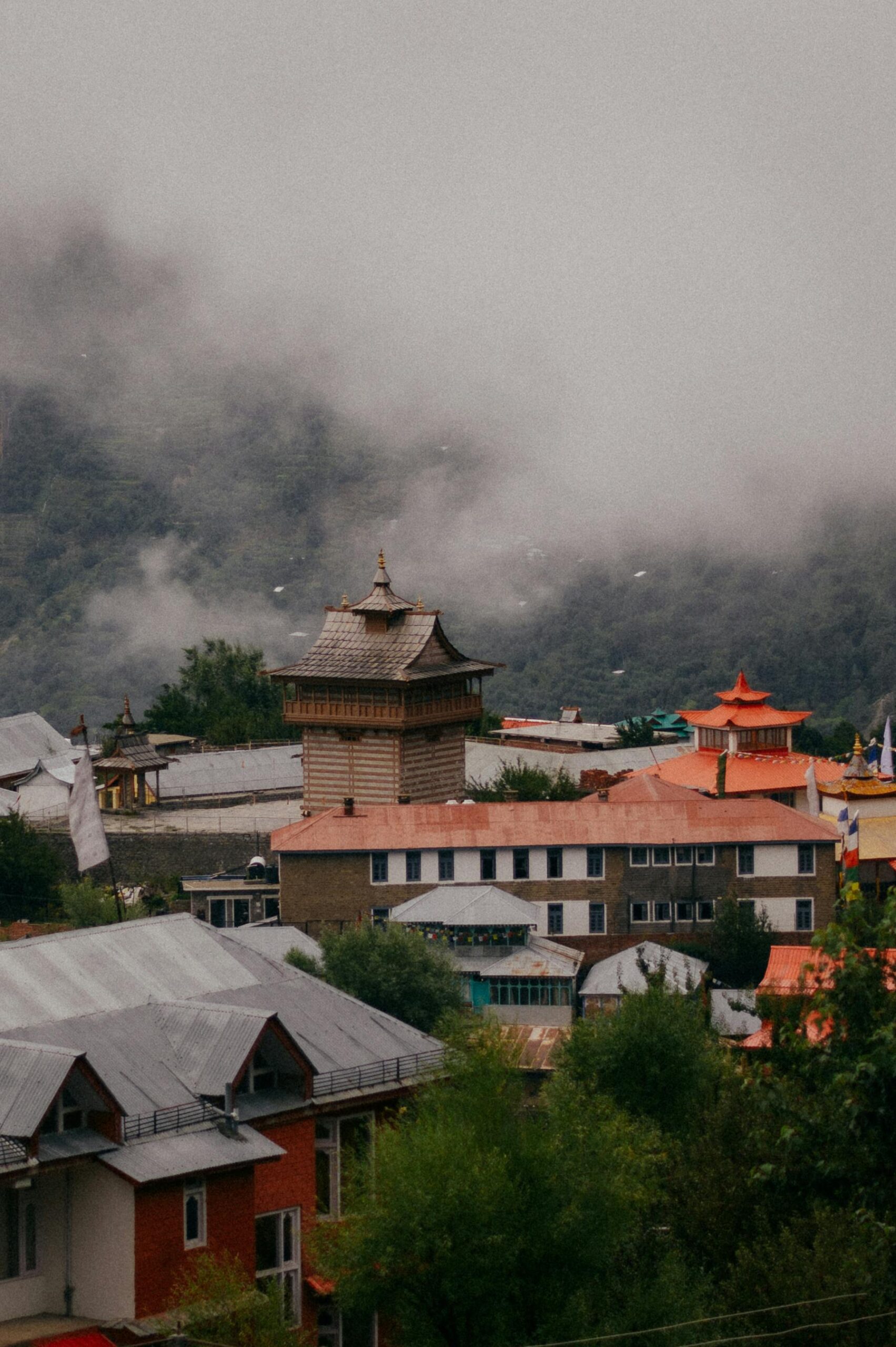 Charming mist-covered town buildings in Reckong Peo with mountains in Himachal Pradesh, India.